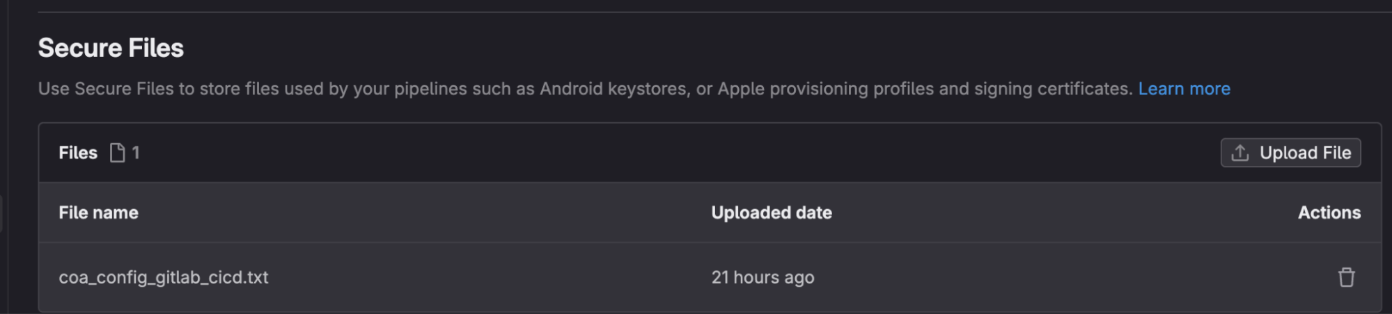 The image shows a section titled Secure Files in a GitLab interface with a dark theme. It explains that Secure Files can be used to store files needed by pipelines, such as Android keystores or Apple provisioning profiles. The section lists one file named coa_config_gitlab_cicd.txt, which was uploaded 21 hours ago, with options to upload a new file or delete the existing one.